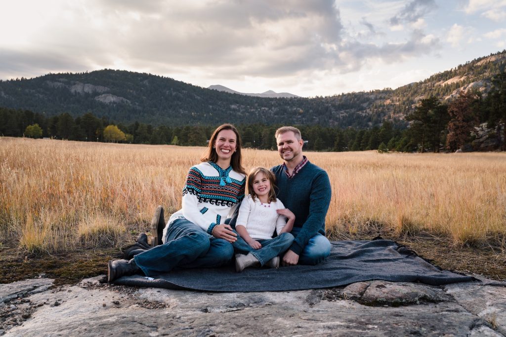 Family of 3 sitting in a field at hildebrand ranch park in littleton colorado for their family photography session